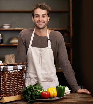 Nutritious and delicious. Portrait of a young man standing in a kitchen with fresh vegetables in front of him.