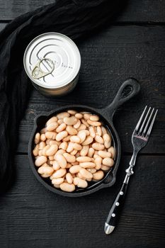 White kidney beans, with metal can, in cast iron frying pan, on black wooden table background, top view flat lay