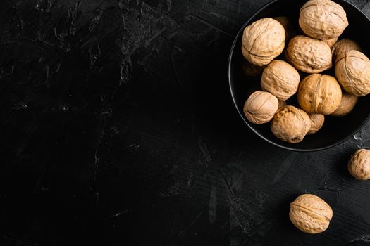 Walnuts with shells, on black dark stone table background, top view flat lay, with copy space for text