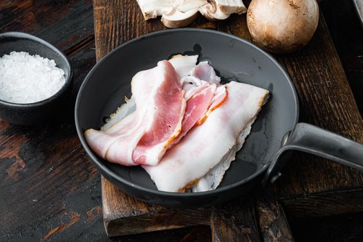 Sizzling bacon pieces in cast iron frying pan, on old dark wooden table background