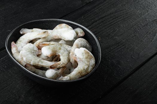 Frozen raw uncooked tiger prawns, shrimps, on black wooden background, with copy space for text