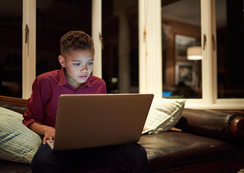 Too much tech too late. Shot of a young boy using a laptop past his bedtime at home.