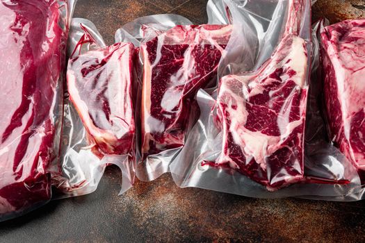 Vacuum packed organic raw beef classic cuts, tomahawk, t bone, club steak, rib eye and tenderloin cuts, on old dark rustic background