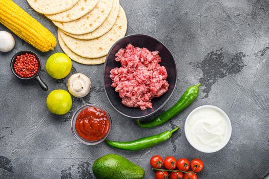 Traditional homemade taco ingredients with meat over grey background, top view.