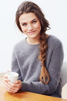 Serene morning. Portrait of a young woman holding a coffee cup and smiling at the camera.