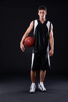 Lets play ball. Full length studio portrait of a basketball player standing with his ball against a black background.
