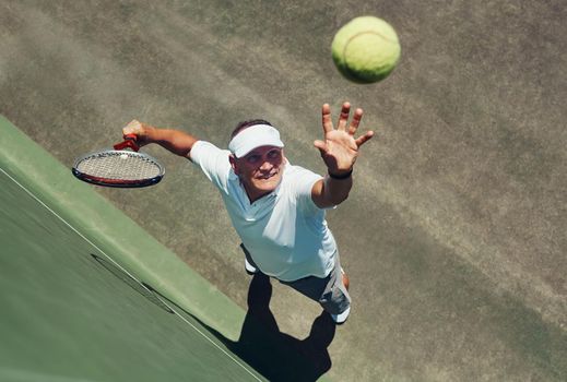 Reach for the sky. High angle shot of a focused middle aged man playing tennis while about to serve the ball to his opponent outside during the day.