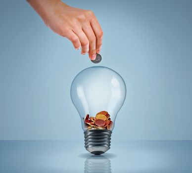 Electricity eating up your savings. Studio shot of a womans hand putting money into a lightbulb.