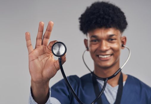 First we diagnose and then we heal. Shot of a male nurse holding up a stethoscope while standing against a grey background.