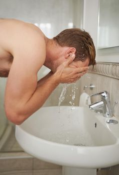 Waking up with a cold splash. A handsome man washing his face in a bathroom.