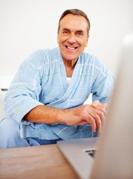 Cheerful pensioner in bathrobe sitting in front of laptop. Portrait of a cheerful pensioner in bathrobe sitting in front of laptop.