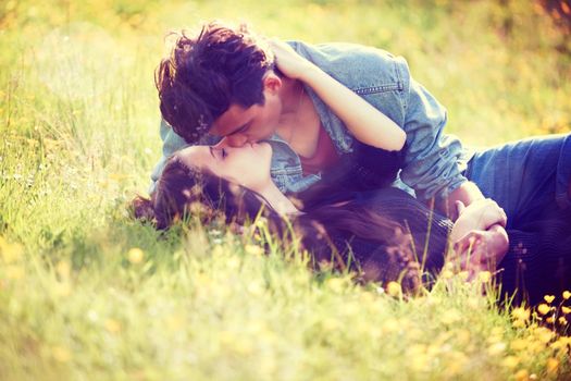 Youthful romance. Vintage style image of a young couple kissing romantically in a summer field.
