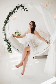 Gorgeous pregnant woman in white gown on designed chair.