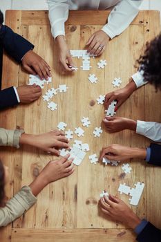 The bigger picture can only be seen with everyones effort. High angle shot of a group of unrecognisable businesspeople building a puzzle together.