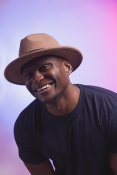 Smiling happy american african man wear stylish hat on pink and purple background. Festive and party concept