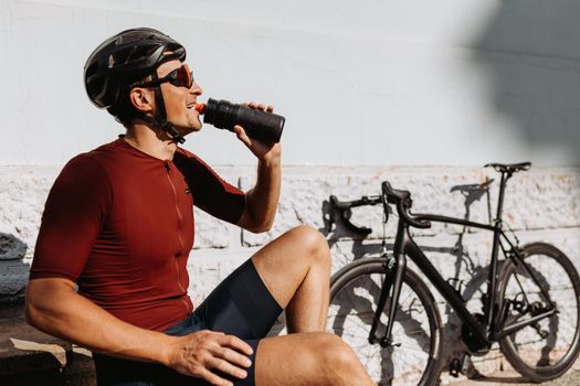Cyclist drinking water while sitting near bike outdoors