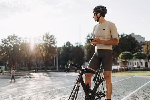 Cyclist in sportswear sitting on bike and using smartphone