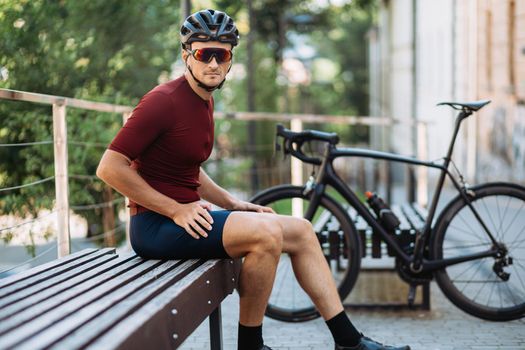 Muscular cyclist resting on bench near bike outdoors