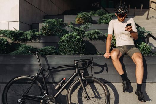Sportsman using smartphone while sitting near bike