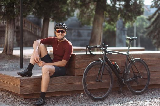 Sporty man in helmet sitting on bench near bike outdoors