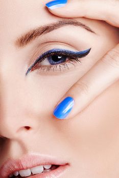 Blue brings out the eyes. Close up of a blue eye with blue eyeliner with two fingers with blue nailpolish on.