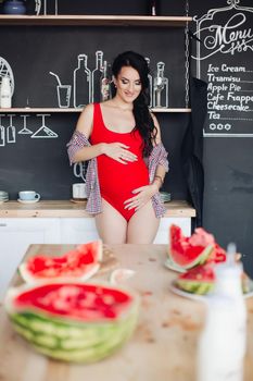 Halved bright watermelon on wooden table against unfocused pregnant woman.