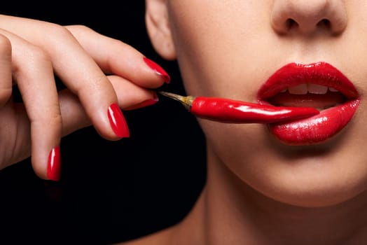 The other forbidden fruit. Closeup of a woman holding a red chilli to her mouth.