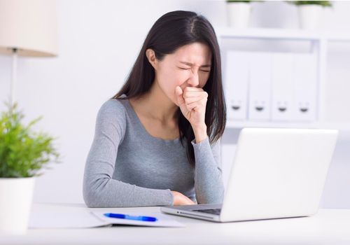 Sick young woman busy at laptop cough struggle with coronavirus or flu at workplace