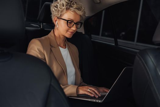 Stylish Business Woman Working on Laptop While Sitting on Back Seat of a Car