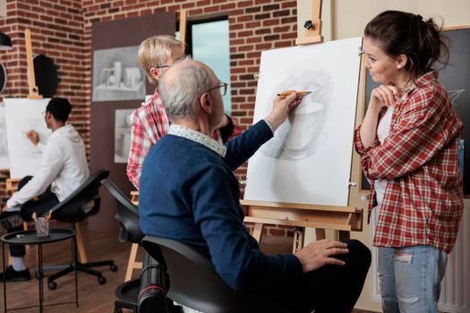 Teacher supervising senior student while drawing vase model on canvas