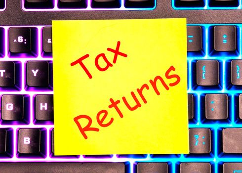 tax returns text written on a yellow sticker lies on a glowing keyboard