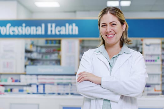 Portrait of a young pharmacist smiling and posing with her arms folded in a pharmacy.
