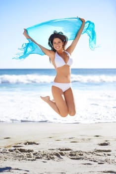 Whimsical and beautiful. Portrait of an attractive young woman jumping happily on the beach.