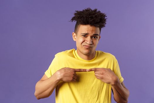 Close-up portrait of shy and modest young silly hispanic man trying say something but being too insecure, grimacing and frowning, look timid, two fingers touching pose, purple background