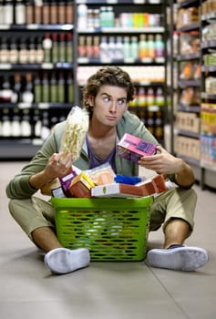 Which one do I need more. A young man sitting on the floor anxiously overwhelmed by grocery shopping.