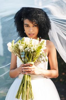 Portrait of a happy and beautiful young bride holding a bouquet of flowers while posing outdoors on her wedding day.