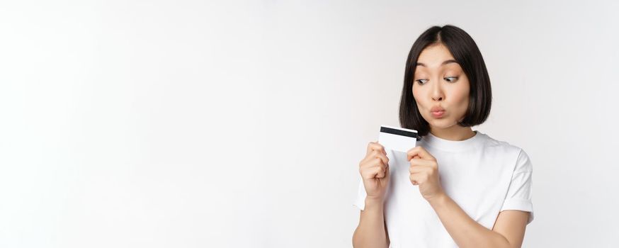 Money and finance concept. Cute japanese girl kissing her credit card, standing in tshirt over white background
