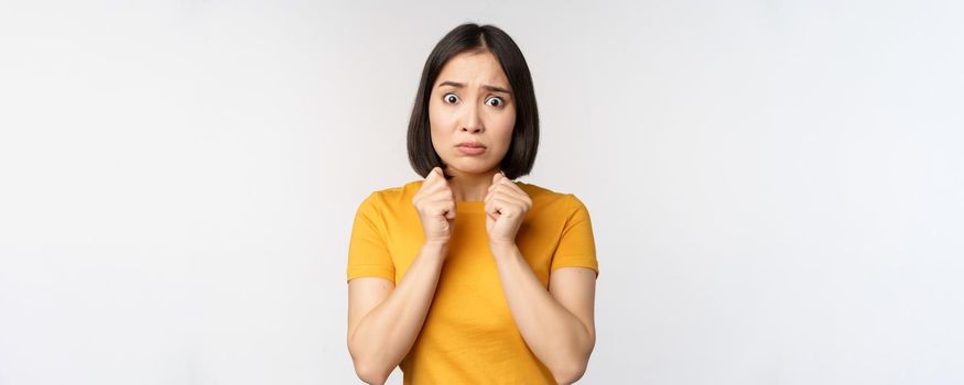 Portrait of scared asian woman shaking from fear, looking terrified and concerned, standing anxious against white background