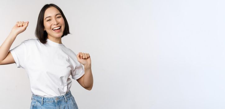 Happy dancing korean girl posing against white background, wearing tshirt