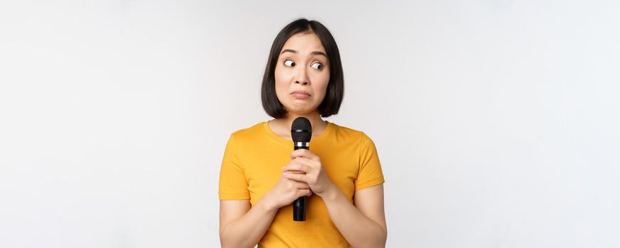 Modest asian girl holding microphone, scared talking in public, standing against white background