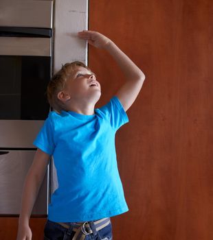 Hes growing fast. A young boy measuring his height at home.