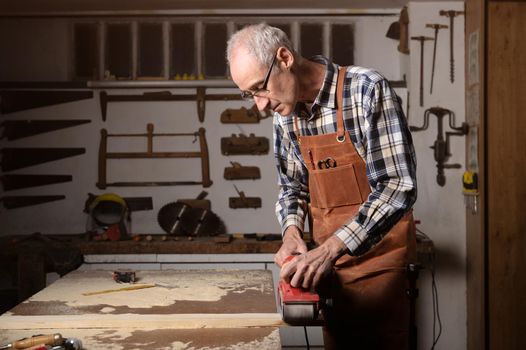 Carpenter sanding wood with belt sander at workshop in wooden board project or woodworking carpentry