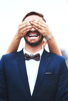I only see fun times ahead with you my love. Shot of a happy bridegroom getting his eyes covered by his bride on their wedding day.