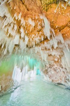 Ice cavern on frozen lake with blue icicles and rocky ceiling