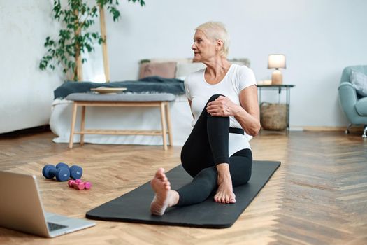 elderly woman performing pilates gymnastics online in her living room.