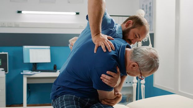 Osteopath helping senior man to crack back bones in cabinet