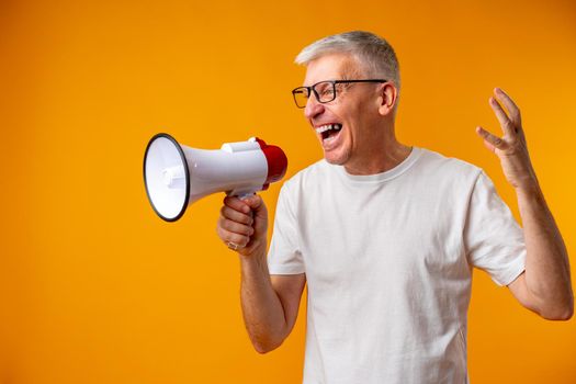 Portrait of mature man shouting with megaphone against yellow background