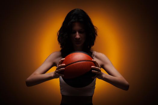 Teenage girl with basketball. Studio portrait on orange colored background..