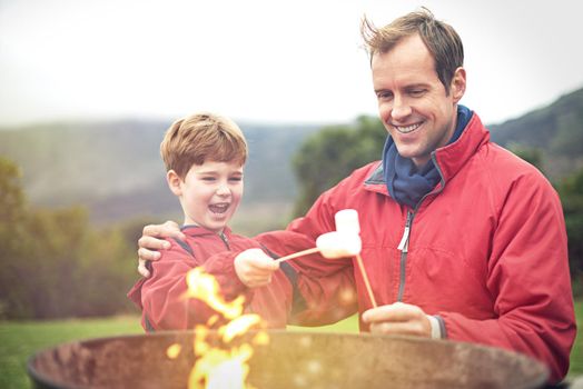 Cant wait to eat them. Shot of a father and son roasting marshmallows over a fire.