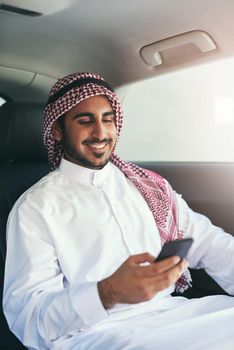 En route to success. Shot of a young muslim businessman using his phone while traveling in a car.